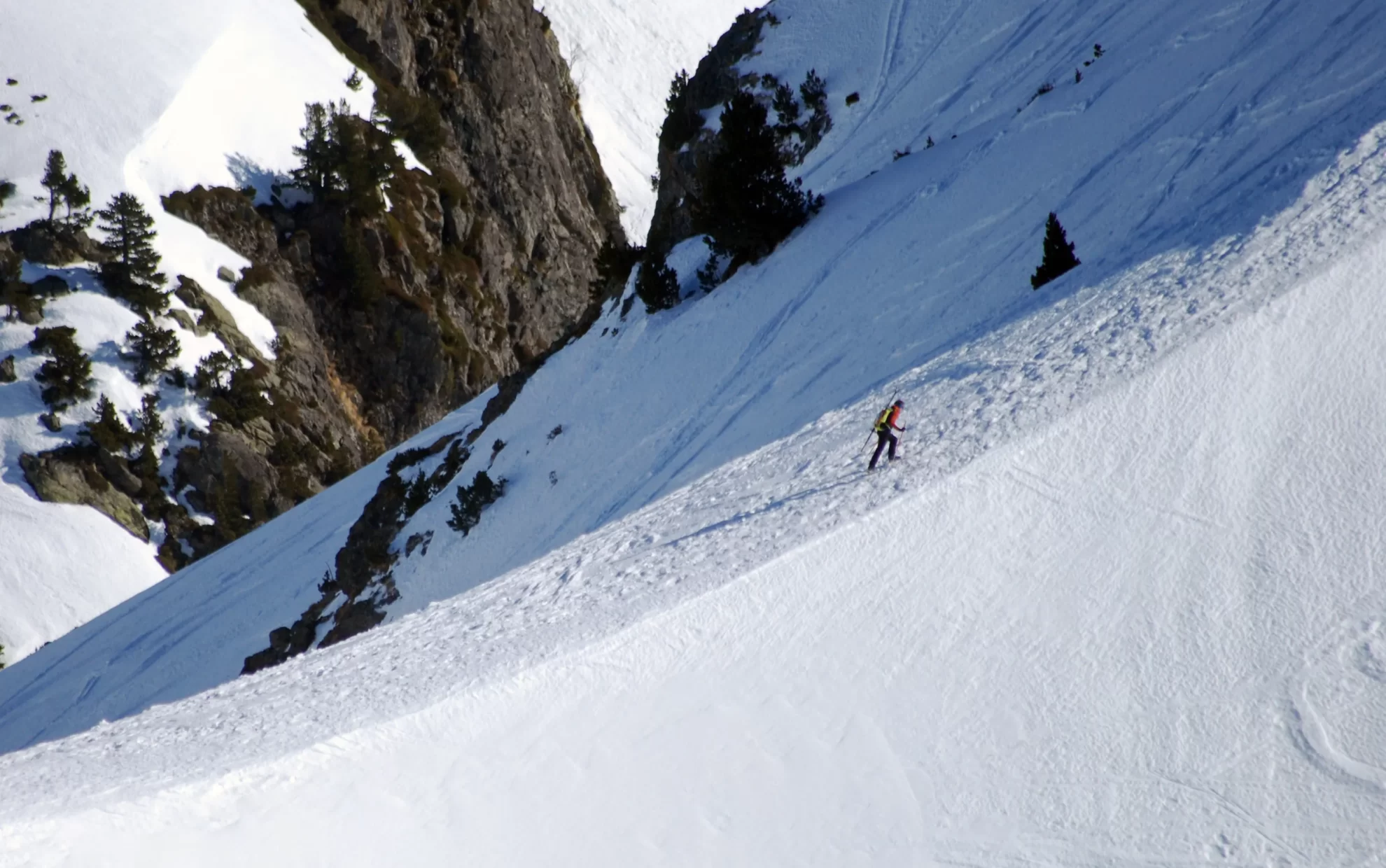Skieur avec des skis sur le sac à dos en train de remonter une vire neigeuse dans un cadre montagnard et enneigée